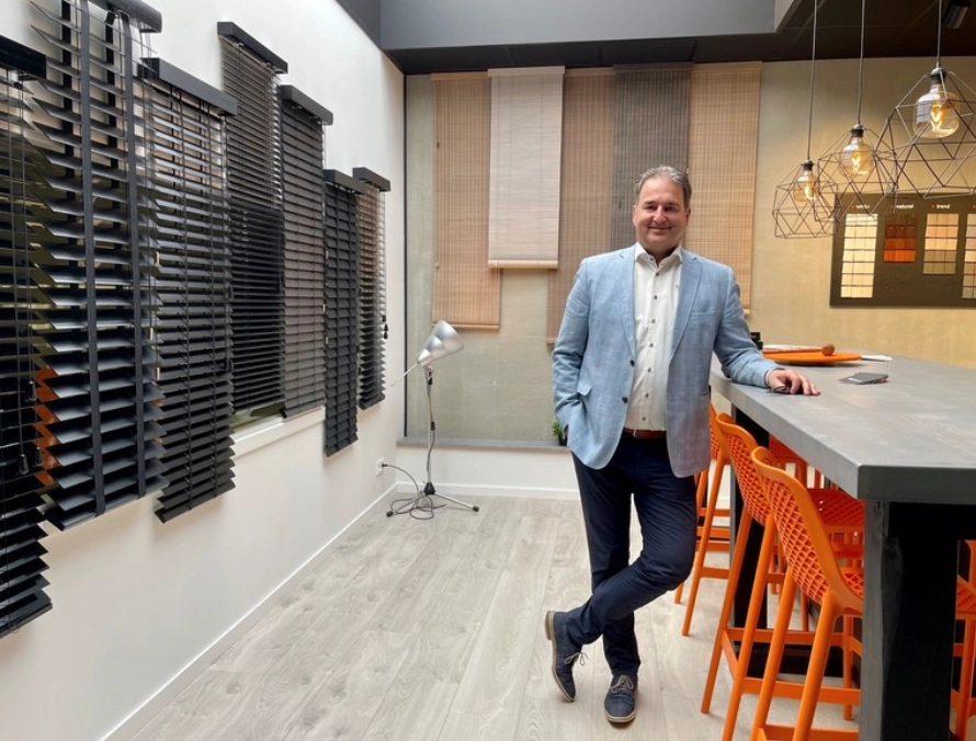 Jos in de showroom van MJ Vloer & Blind in Maaseik, met houten jaloezie&euml;n en rolgordijnen aan de wand